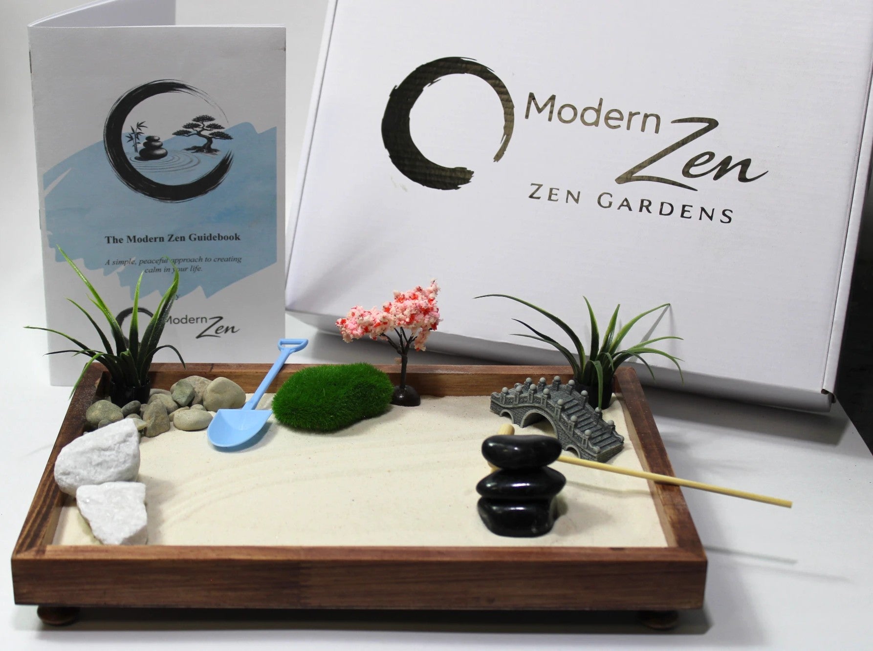 Zen garden set with sand, rocks, plants, and tools in front of a 'Modern Zen' branded backdrop.