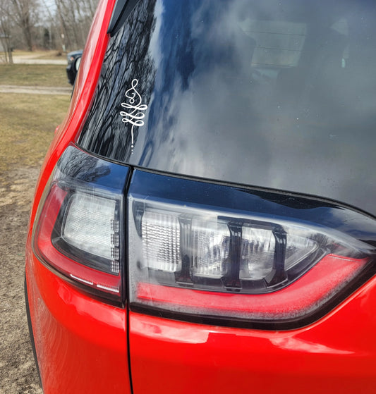 Close-up of a red car's back window with an unalome white decal 